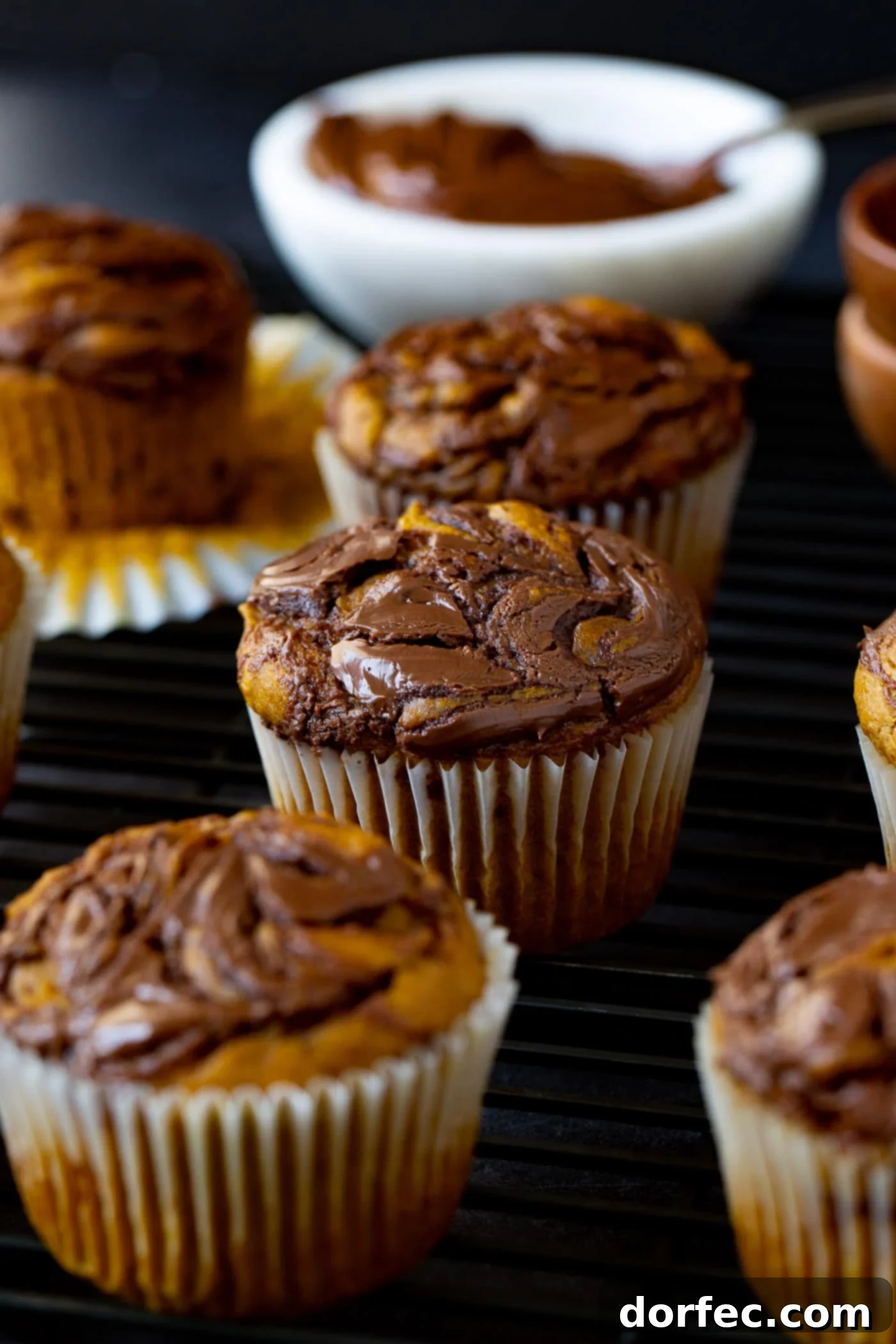 Delicious Nutella Swirled Pumpkin Muffins A close-up of a perfectly baked Nutella swirled pumpkin muffin. The paper liner is peeled back, showcasing the warm, spiced pumpkin muffin batter elegantly marbled with rich, dark Nutella swirls, creating a stunning visual and delicious flavor combination.