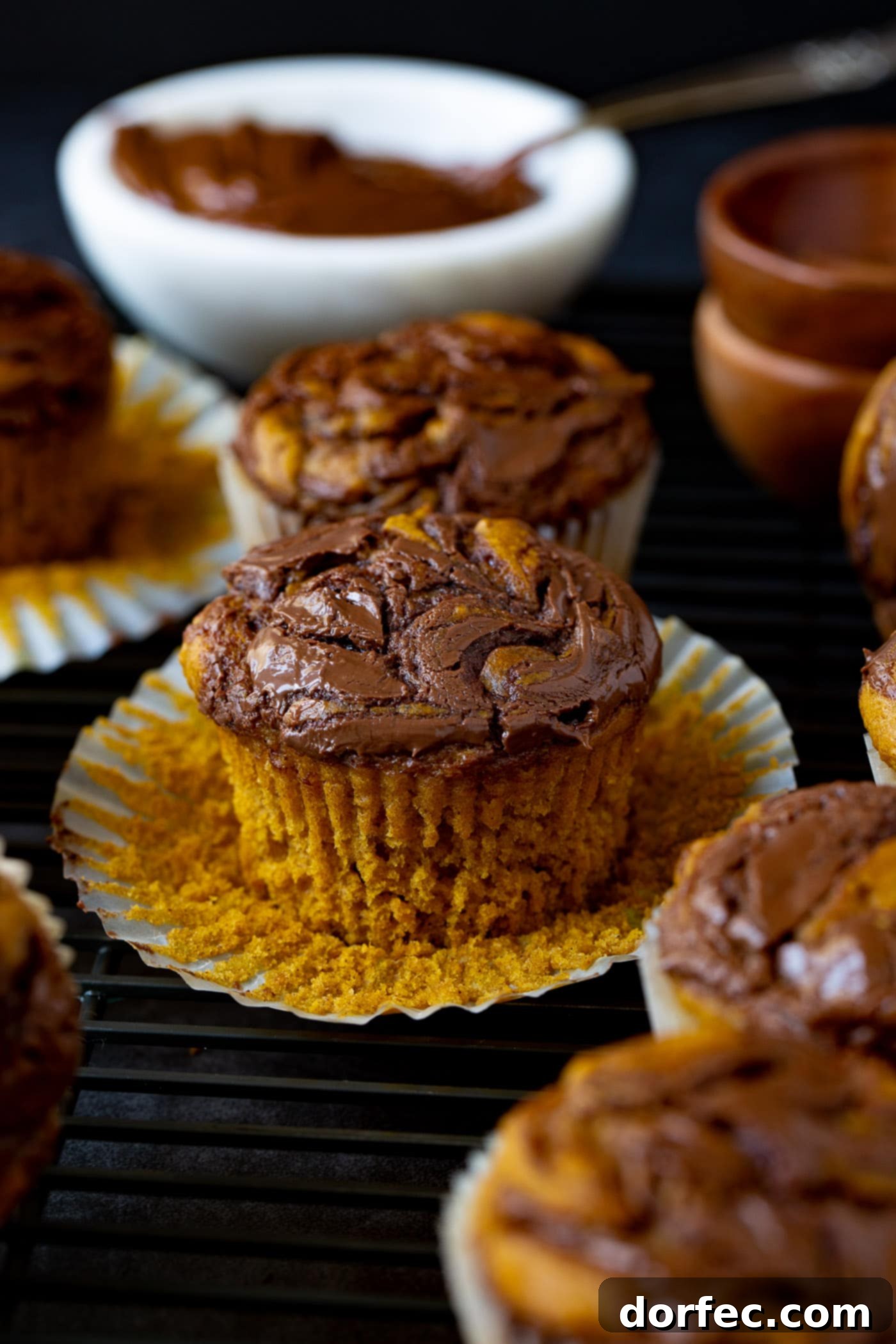 Perfectly Moist Nutella Swirled Pumpkin Muffins Close-up of freshly baked Nutella swirled pumpkin muffins. The paper liners are peeled back on several muffins, revealing the soft, golden-orange pumpkin interior beautifully marbled with streaks of dark, rich Nutella. They look incredibly inviting and delicious.