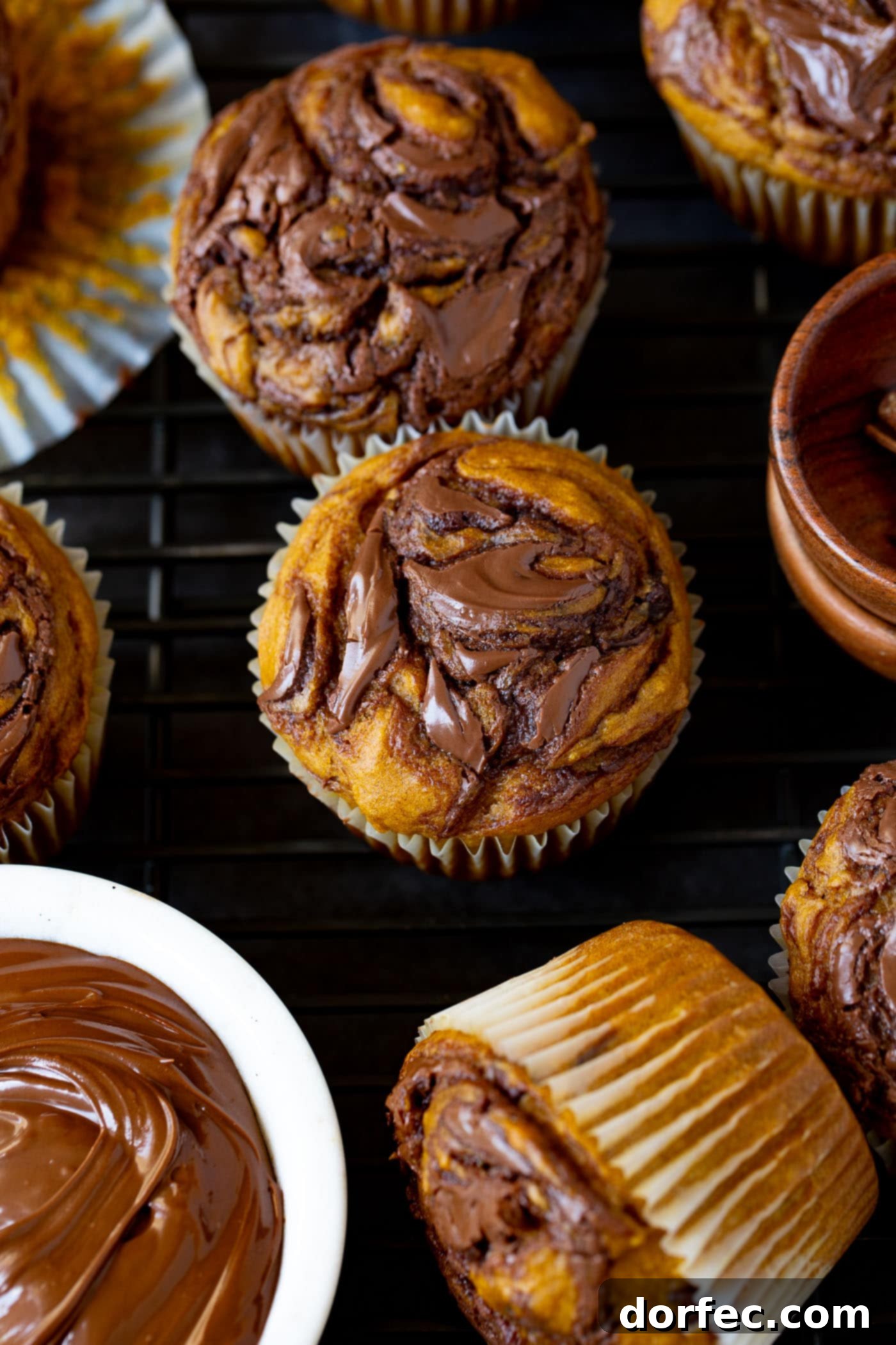 Homemade Nutella Swirled Pumpkin Muffins Nutella swirled pumpkin muffins showcasing the beautiful marbling of chocolate-hazelnut spread within the golden pumpkin batter. A small bowl of Nutella sits enticingly next to the baked muffins, inviting another delicious swirl.