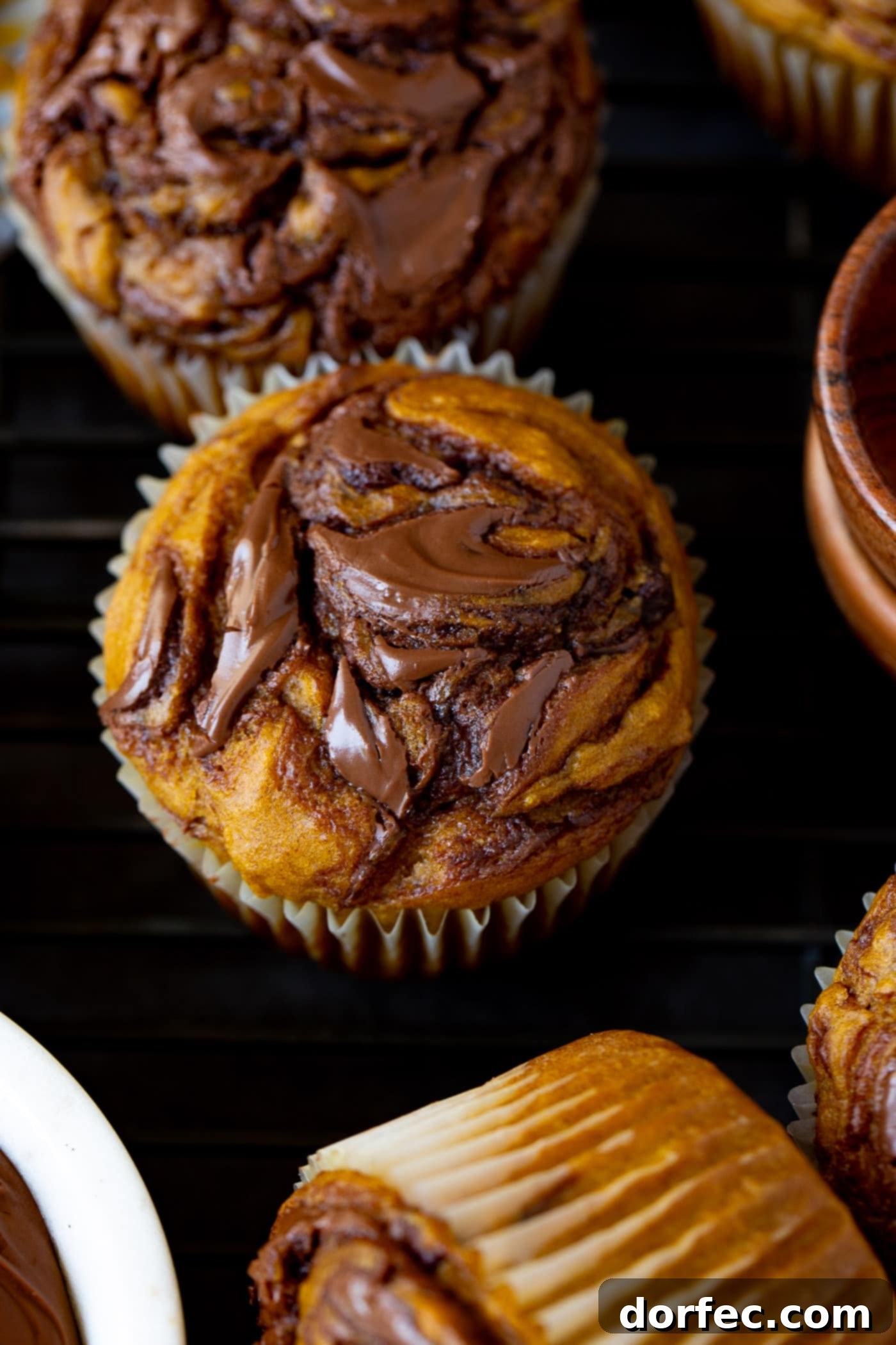 Top View of Nutella Swirled Pumpkin Muffins A top-down view of a single Nutella swirled pumpkin muffin, perfectly baked and displaying beautiful swirls of dark Nutella through its golden pumpkin base. Other equally delicious muffins are visible, slightly blurred, in the background.