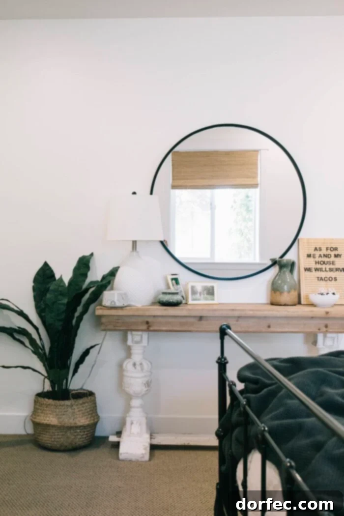 A sleek Urban Outfitters Black Round Mirror positioned above a simple side table, accented by a modern floor plant, creating a contemporary and inviting bedroom vignette.