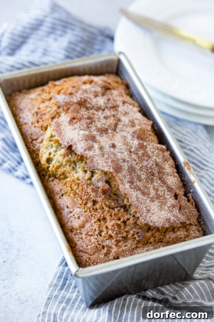 A loaf of moist zucchini bread in a bread pan, ready to be sliced