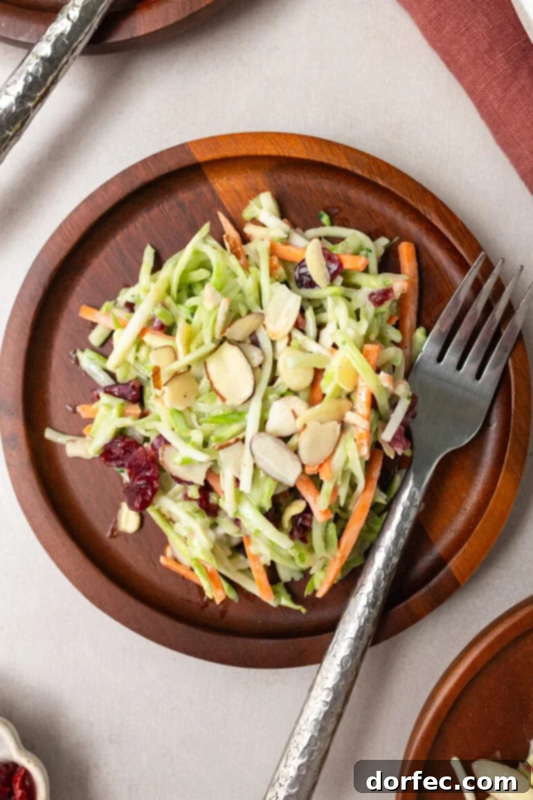 A close-up of a serving of broccoli slaw on a small wooden plate, with a fork resting beside it.