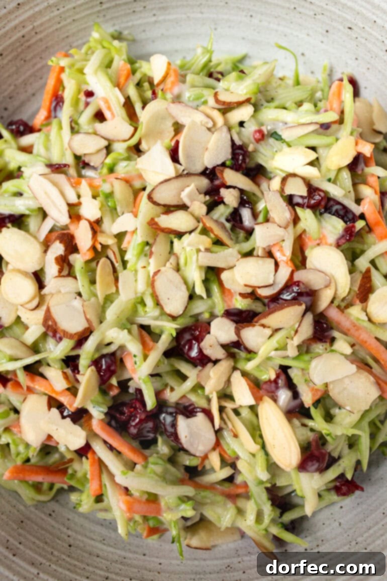 A large bowl of broccoli slaw, featuring shredded broccoli stems, carrots, craisins, and sliced almonds, all coated in a creamy, homemade dressing.