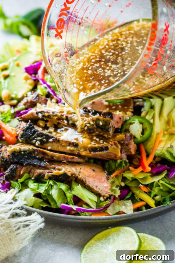 Zesty Thai Peanut Salad with Grilled Flank Steak 2 A beautifully arranged plate of Healthy Thai Peanut Salad with Grilled Flank Steak. A creamy ginger dressing is being artfully drizzled over the vibrant ingredients, including mixed greens, colorful vegetables, and tender, marinated flank steak.