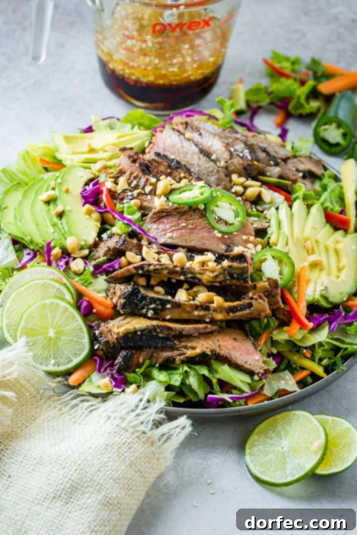 Zesty Thai Peanut Salad with Grilled Flank Steak 4 A vibrant and artfully styled plate of Healthy Thai Peanut Salad with Grilled Flank Steak, featuring fresh mixed greens, colorful vegetables, and tender, peanut sauce-marinated steak. Garnished with fresh lime, avocado, and jalapeño slices, alongside a ginger dressing and sesame seeds.