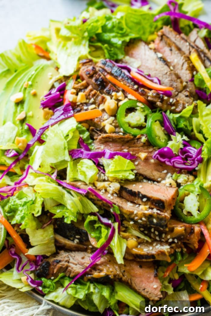 Zesty Thai Peanut Salad with Grilled Flank Steak 6 A vibrant plate brimming with mixed greens, fresh vegetables, and tender, creamy nut-based sauce-marinated steak, generously drizzled with a zesty ginger dressing and sprinkled with sesame seeds.