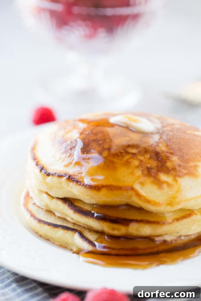 A stack of fluffy sour cream pancakes with a little butter melting on top and a drizzle of syrup dripping down the side. Our recipe for melt in your mouth sour cream pancakes