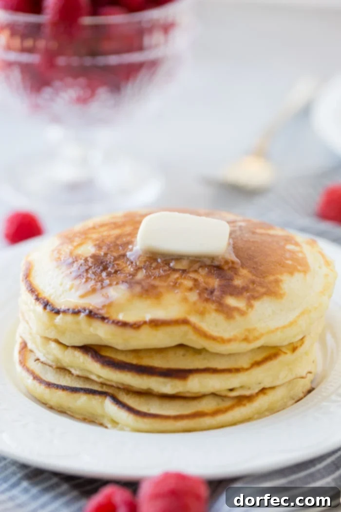 A stack of fluffy homemade sour cream pancakes with a little butter melting on top and a drizzle of syrup dripping down the side. Our recipe for melt in your mouth sour cream pancakes