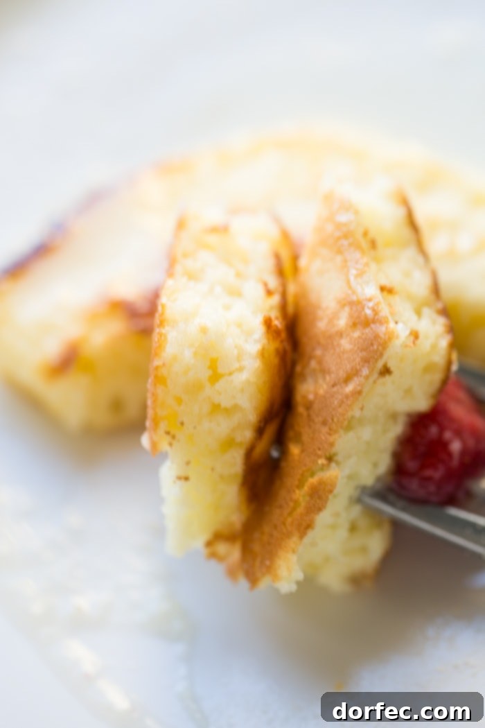 a couple of pieces of cut melt in your mouth sour cream pancakes on a fork with a small raspberry