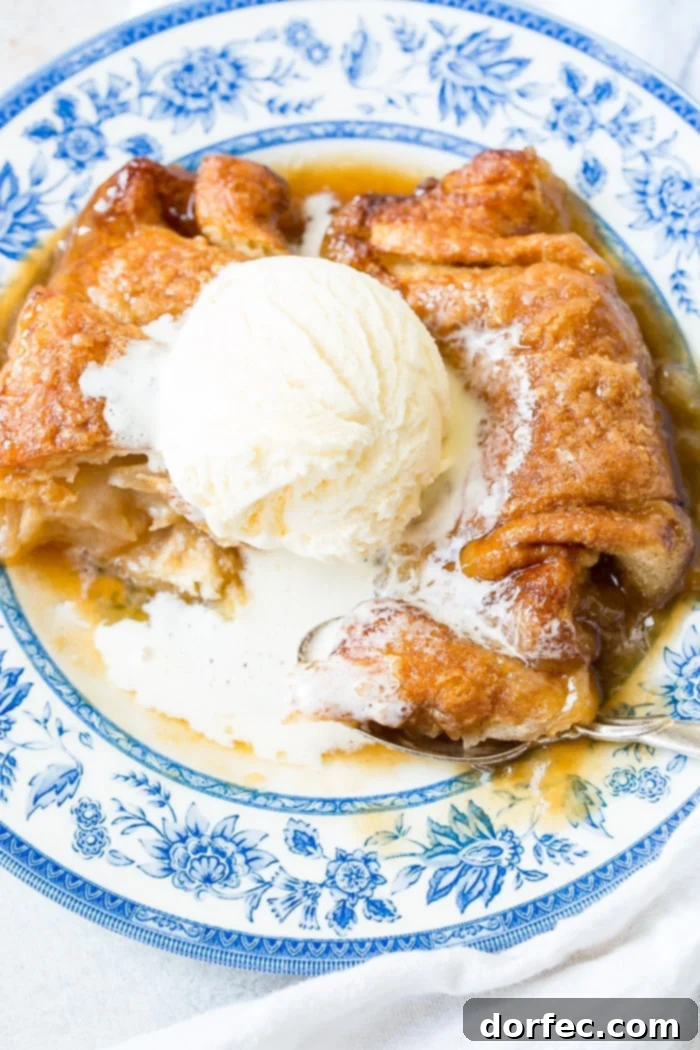 Sweet Simple Sprite Apple Dumplings 3 A second view of two apple dumplings, richly coated in caramel sauce, served with a scoop of vanilla ice cream on a blue and white china plate.