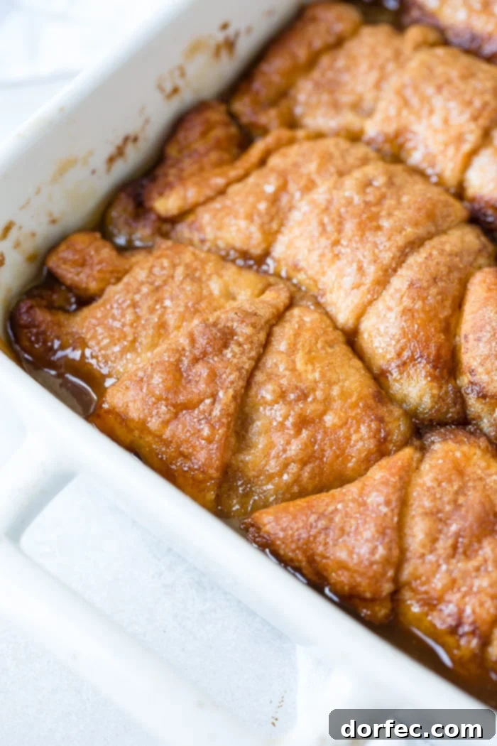 Sweet Simple Sprite Apple Dumplings 4 A white ceramic casserole dish filled with baked apple dumplings, golden brown and bubbling with a rich, caramelized sauce.