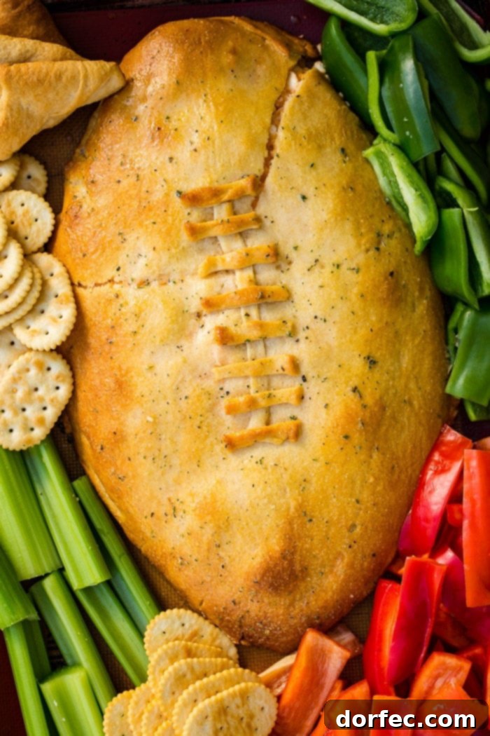 A cookie sheet with crackers, celery, peppers, and a football made out of crescent rolls and stuffed with buffalo chicken dip recipe