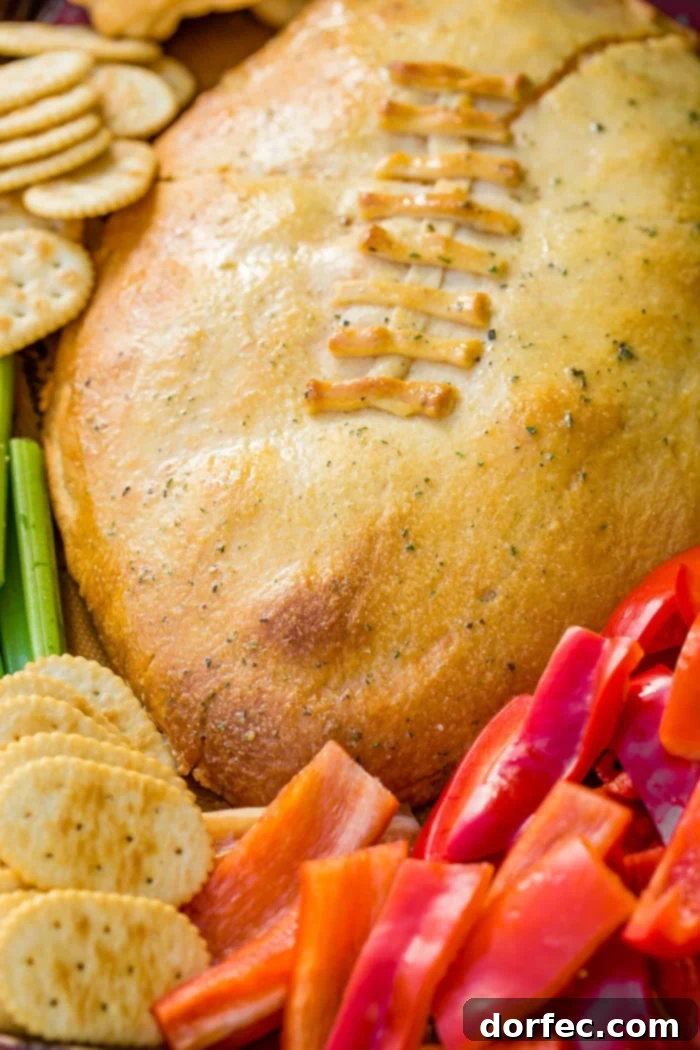 A cookie sheet with crackers, celery, peppers, and a football made out of crescent rolls and stuffed with buffalo chicken dip recipe