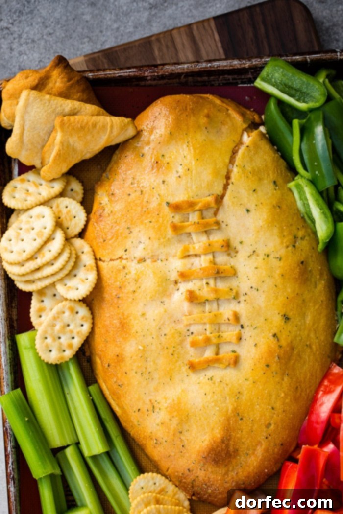 A cookie sheet with crackers, celery, peppers, and a football made out of crescent rolls and stuffed with buffalo chicken dip recipe