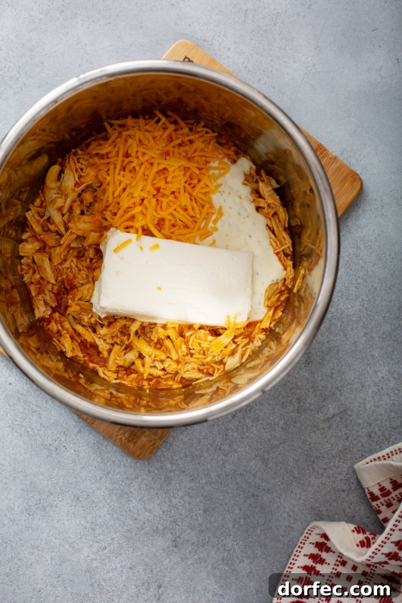 The inner pot of an Instant Pot shows a rich mixture of shredded chicken, melted cream cheese, shredded cheddar cheese, and buffalo sauce, all combined into a luscious dip.