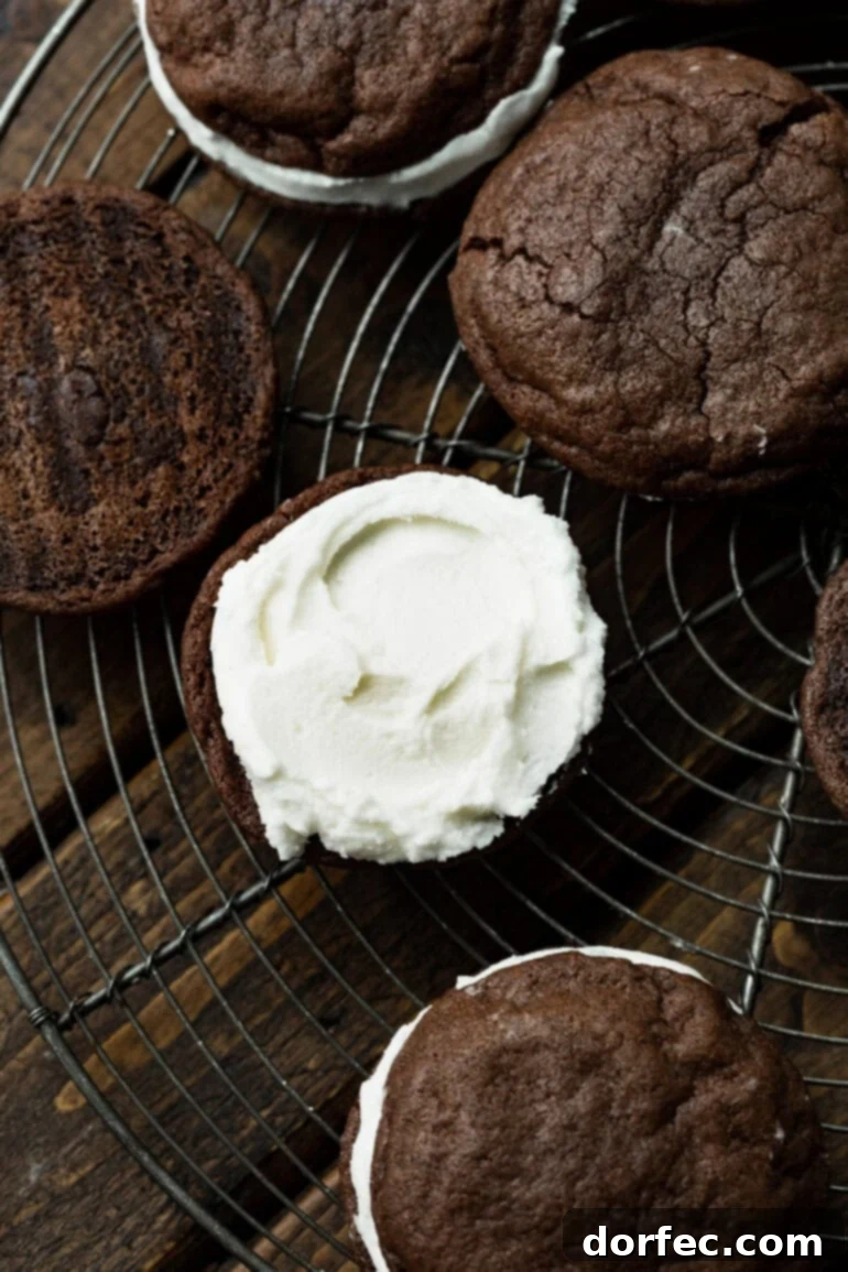 A photo of a frosted chocolate cookie sitting on a circular wire cooling rack, ready to be topped with another cookie.