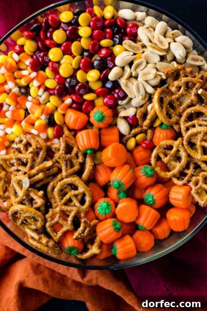 A vibrant glass bowl overflowing with a delicious mix of candy corn, crunchy pretzels, colorful M&Ms, savory peanuts, and festive candy pumpkins, perfect for a Halloween celebration.