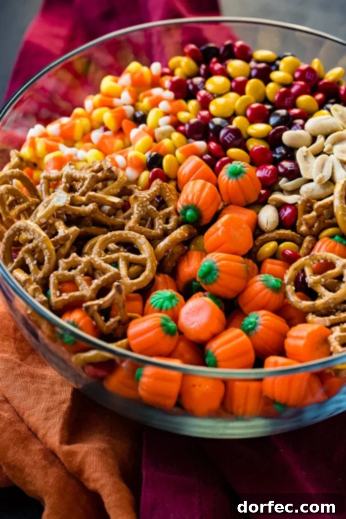 A close-up shot of a glass bowl filled with a festive 5-Minute Halloween Snack Mix, showcasing crunchy pretzels, sweet candy corn, colorful M&Ms, roasted peanuts, and cheerful candy pumpkins, ready for any celebration.