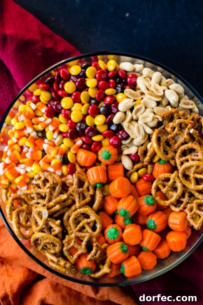 A festive clear glass bowl filled with a delightful Halloween Snack Mix, featuring a colorful assortment of candy corn, salted peanuts, Halloween-themed M&Ms, crunchy pretzels, and cheerful candy pumpkins, glistening under warm lighting.