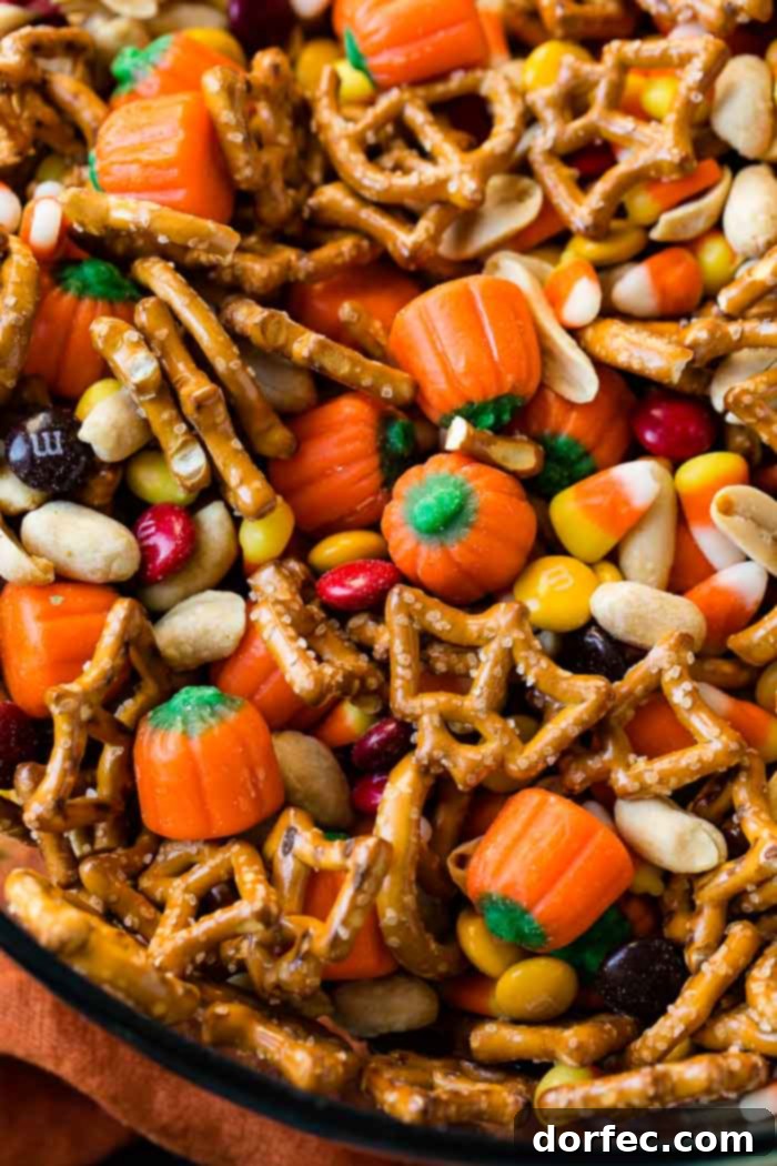 A close-up shot of a glass bowl filled with a delightful 5-Minute Halloween Snack Mix, featuring a colorful blend of candy corn, crunchy pretzels, Halloween-themed M&Ms, salted peanuts, and charming candy pumpkins, ready to be enjoyed.