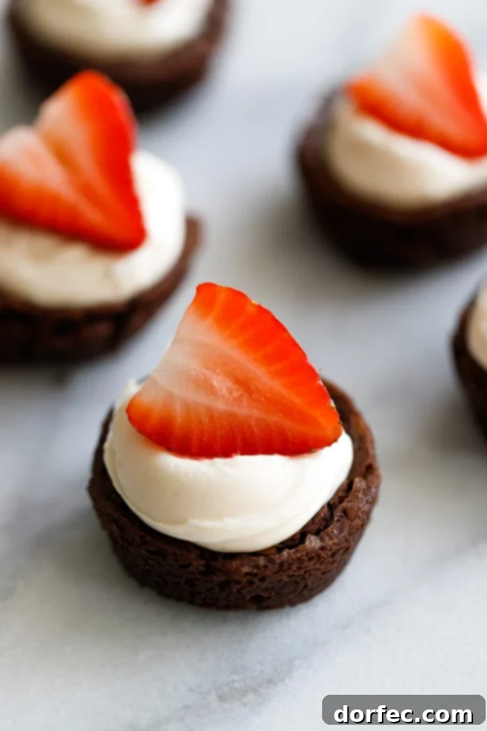 Brownies filled with a cream and topped with a bright red strawberry making elegant strawberry brownie tuxedo cups