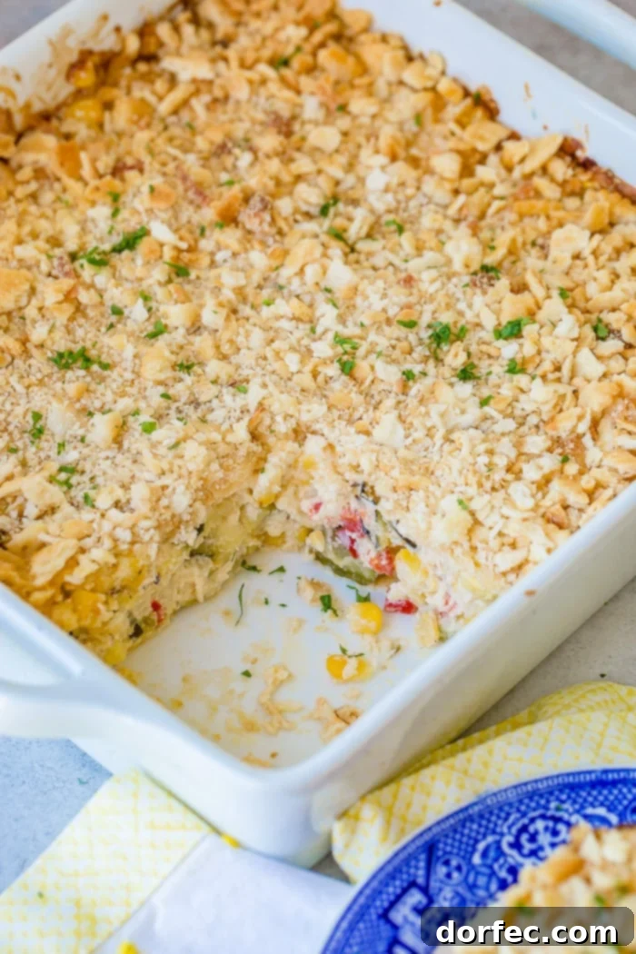 Golden Zucchini Corn Bake 3 A hearty white casserole dish filled with layered cheesy zucchini corn casserole, a slice removed to reveal the delicious interplay of zucchini, corn, peppers, melted cheese, and a golden buttery cracker topping.