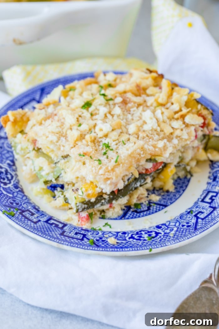 Golden Zucchini Corn Bake 5 A close-up of a slice of cheesy zucchini corn casserole on a blue plate, highlighting the perfectly melted cheese and crisp cracker topping.