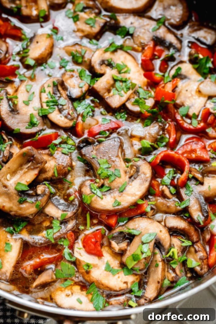 A close-up photo of perfectly sauteed Italian mushrooms with vibrant sliced red peppers and onions, generously topped with freshly chopped parsley, glistening with a savory sauce.