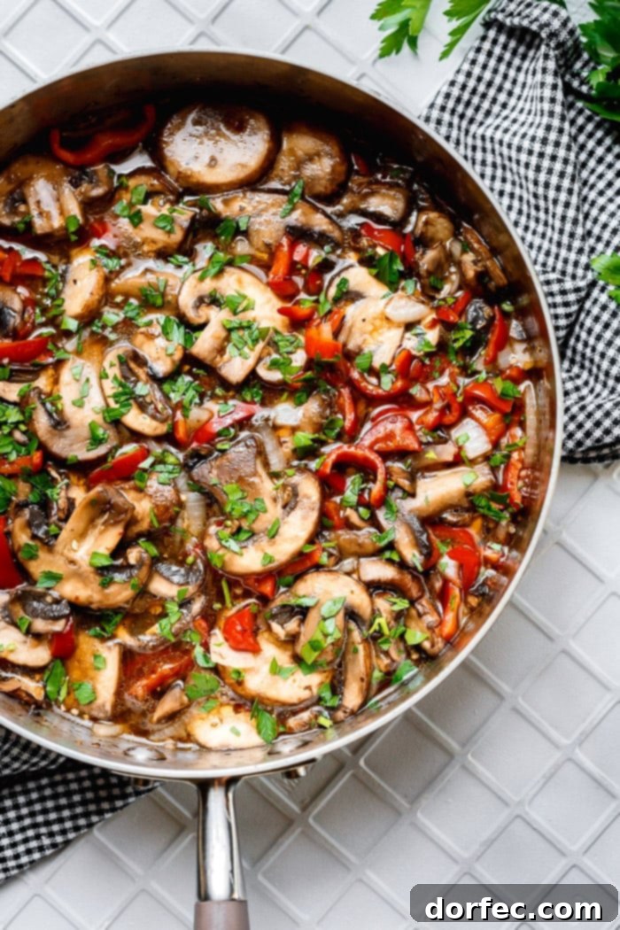 A photo of a deep saute pan filled with sliced sauteed mushrooms, sliced red bell peppers, and diced onions, all topped with chopped fresh parsley, showcasing the vibrant colors and savory goodness of the Italian Sauteed Mushrooms.