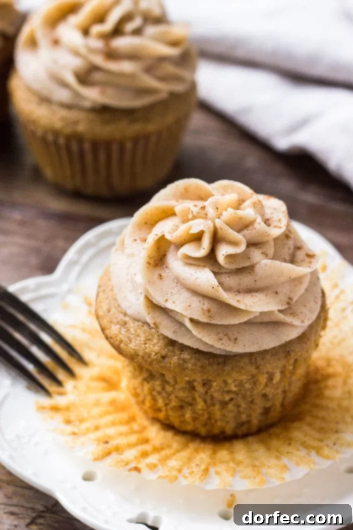 A moist spice cake cupcake topped with cream cheese frosting on a white plate, exuding a warm, inviting glow.