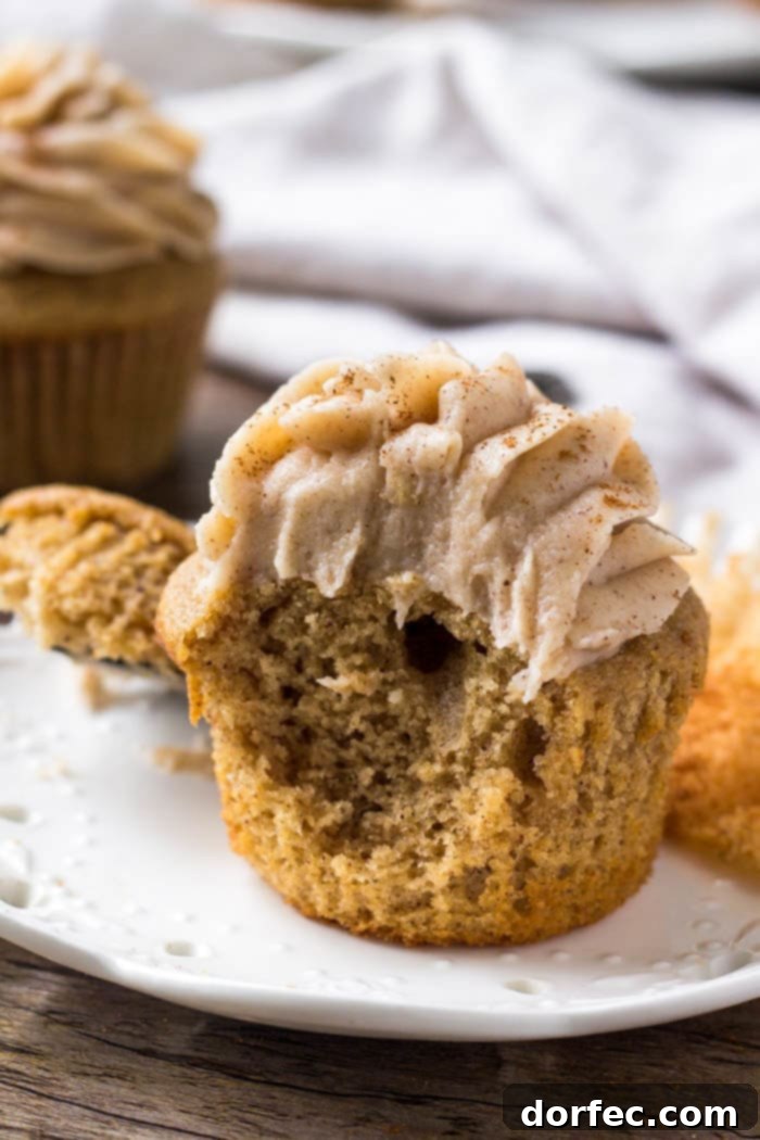 A delicious spice cake cupcake topped with cinnamon cream cheese frosting, with a bite taken out, revealing its moist interior.