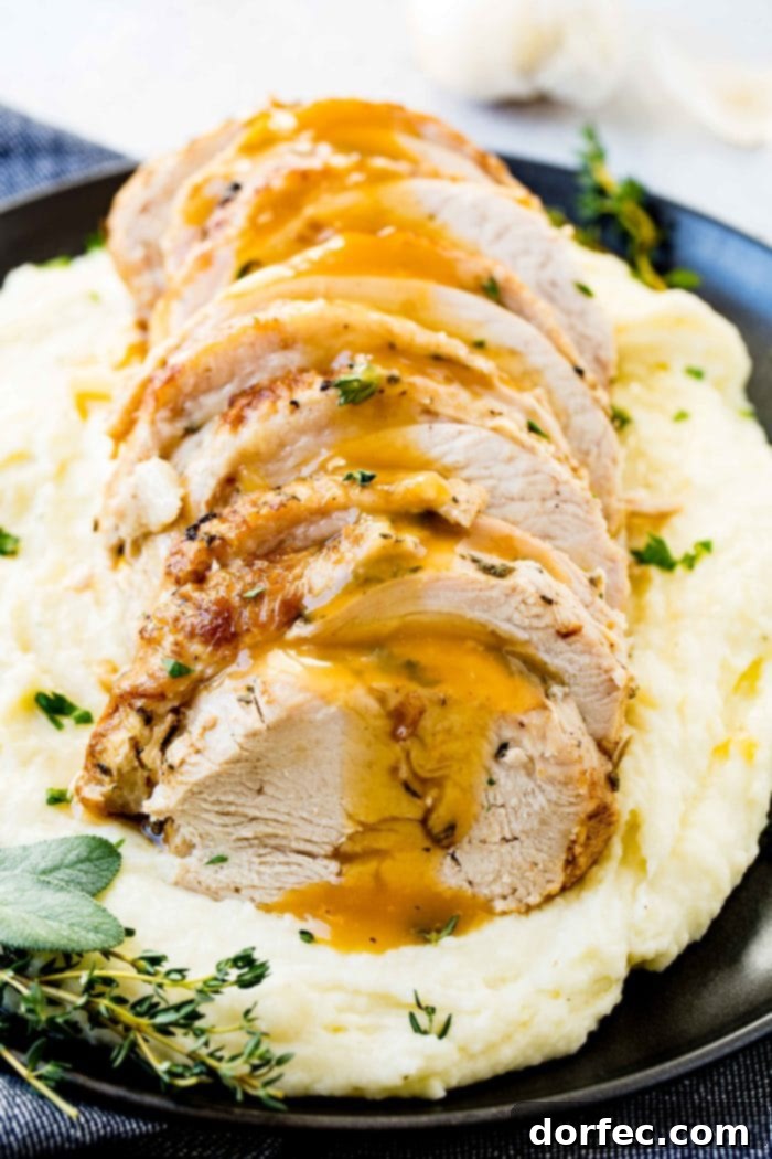 A perfectly sliced Instant Pot turkey breast, generously drizzled with rich homemade gravy and garnished with fresh herbs, resting on a bed of creamy mashed potatoes on an elegant black plate.