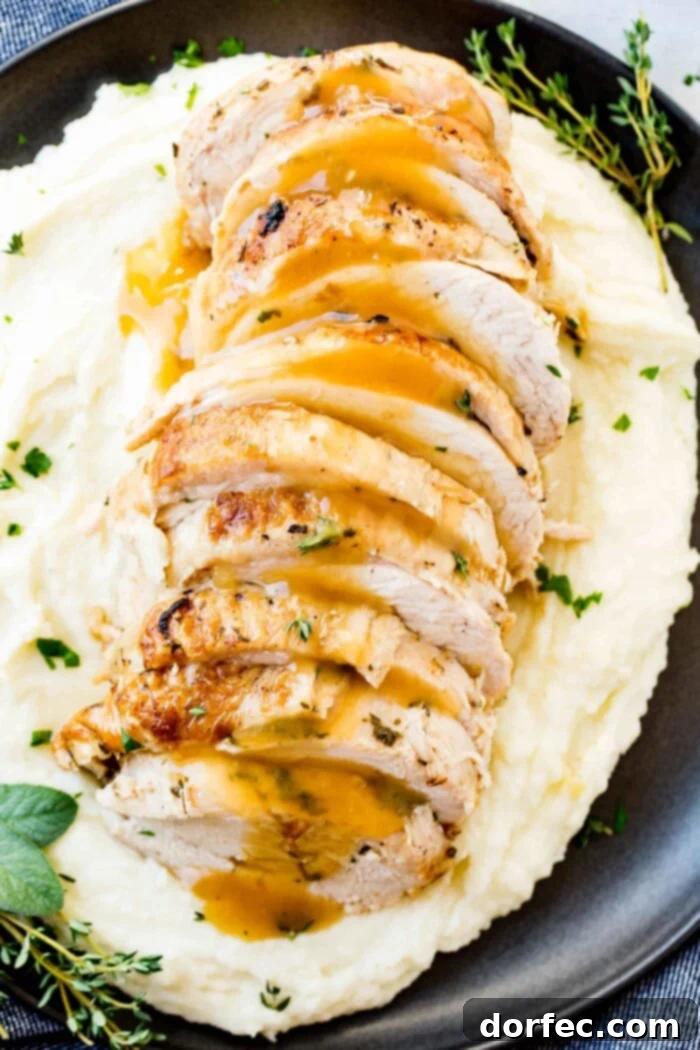 A vibrant close-up of sliced Instant Pot turkey breast, generously coated in rich gravy and adorned with fresh herbs, presented on a bed of fluffy mashed potatoes, all served on a dark plate.