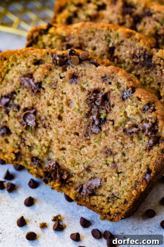 Decadent Chocolate Chip Zucchini Loaf 2 a photo of a slice of chocolate chip zucchini bread with two more slices stacked behind it that are full of mini chocolate chips all sitting on the counter with mini chocolate chips sprinkled on the counter in front of the bead