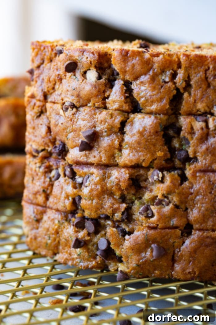 Decadent Chocolate Chip Zucchini Loaf 3 a photo of a stack of four slices of homemade zucchini bread sitting on a gold wire cooling rack with the slices laying on their side looking at the top of the bread which is sprinkled with mini chocolate chips