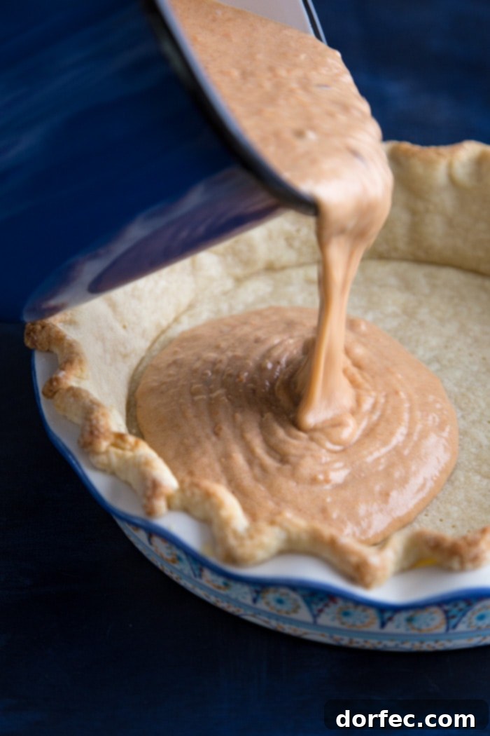 Sweet potato pie filling being meticulously poured into a golden, par-baked pie crust, showcasing the creamy texture before baking.