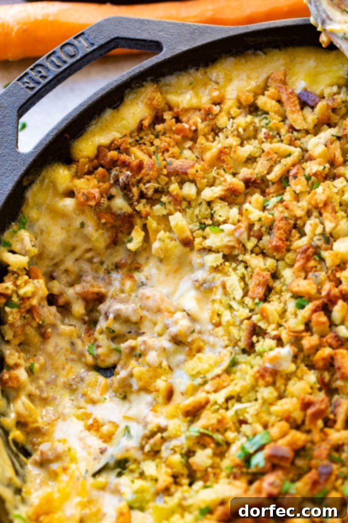 A close-up view of a creamy zucchini sausage casserole with a golden-brown stuffing topping in a cast iron skillet, showing a scoop already taken out, revealing the rich interior.