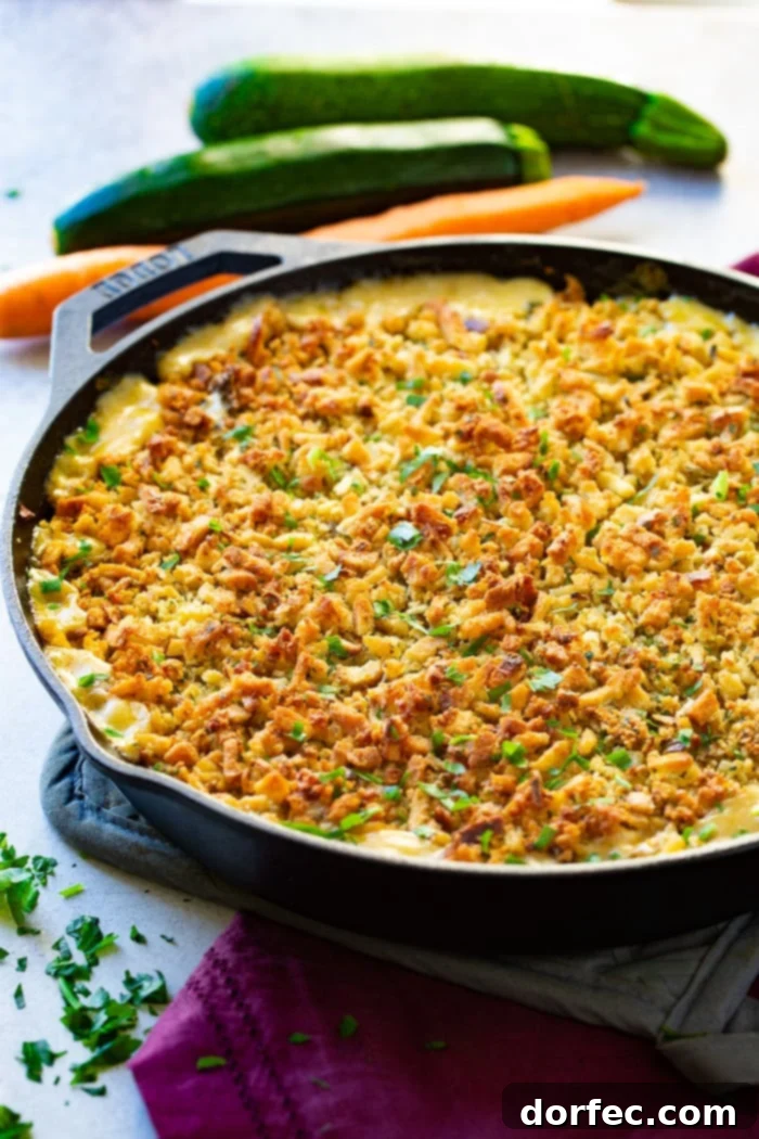 A photo of a creamy casserole in a cast iron skillet, covered in a perfectly toasted stuffing topping, resting on a pot holder with a fresh carrot visible in the background.