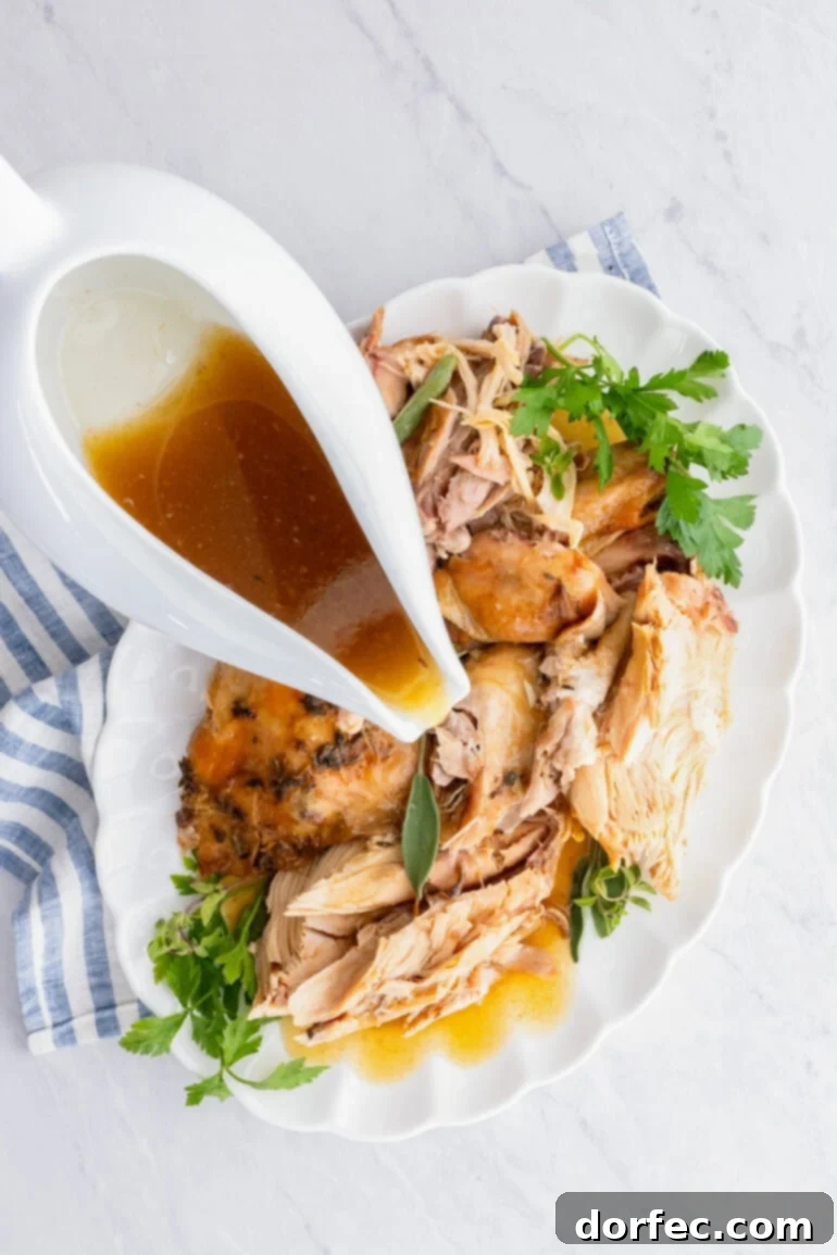 A gravy boat overflowing with rich turkey gravy, positioned over a platter of tender, juicy chunks of turkey, ready to be served.
