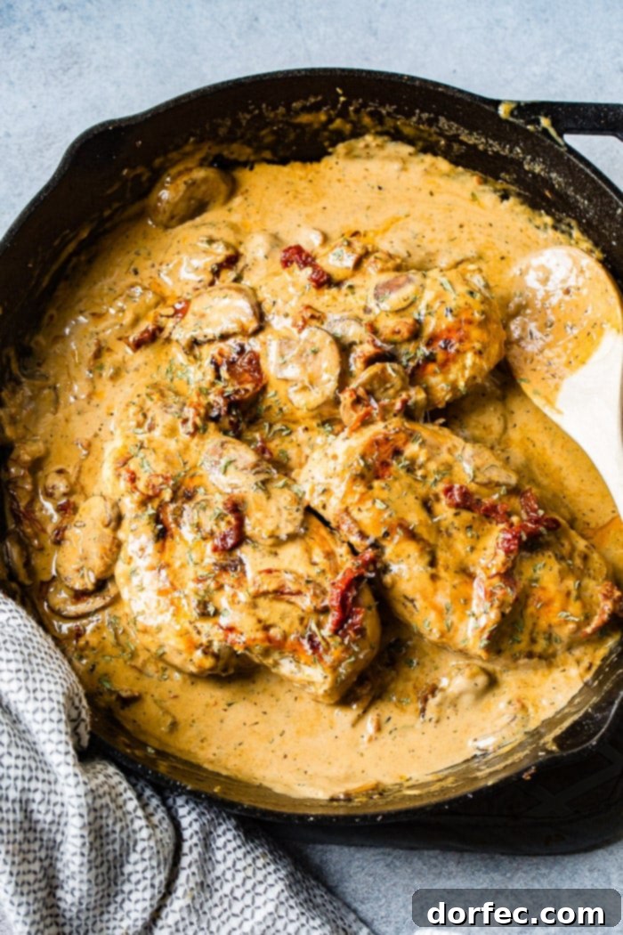 Effortless Creamy Herbed Chicken with Sun-Dried Tomatoes 3 A black cast iron skillet with a creamy sauce full of sun dried tomatoes, mushrooms and seasoning over perfectly cooked chicken
