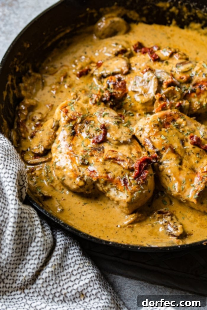 Effortless Creamy Herbed Chicken with Sun-Dried Tomatoes 4 A black cast iron skillet with a creamy sauce full of sun dried tomatoes, mushrooms and seasoning over perfectly cooked chicken