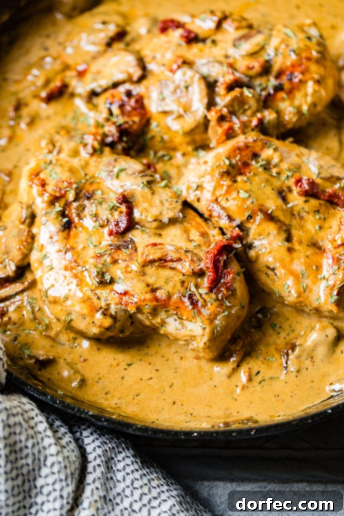 Effortless Creamy Herbed Chicken with Sun-Dried Tomatoes 5 A black cast iron skillet with a creamy sauce full of sun dried tomatoes, mushrooms and seasoning over perfectly cooked chicken
