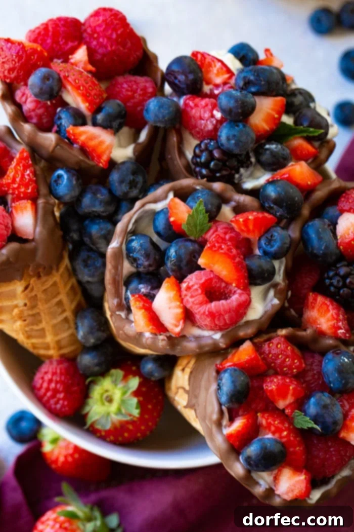 A white bowl with chocolate dipped cones filled with yogurt and fresh berries.