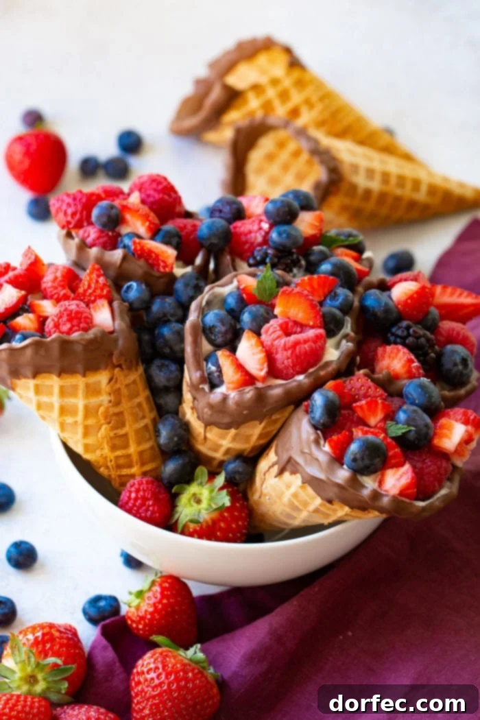 A bowl of waffle cones filled with yogurt, strawberries, blueberries & raspberries with 2 waffle cones in the background.