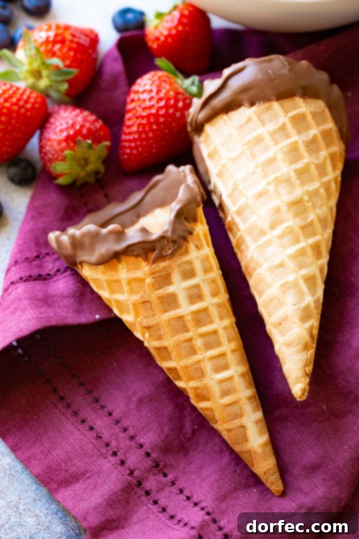 2 waffle cones dipped in chocolate with berries on a purple linen.
