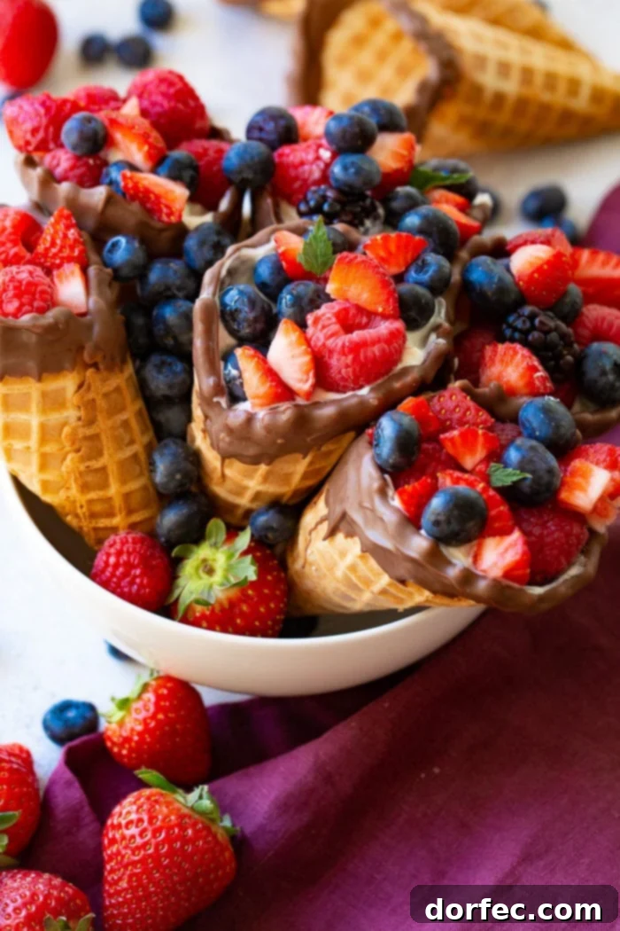 A white bowl filled with waffle cone fruit and yogurt cups with a purple linen and more berries.