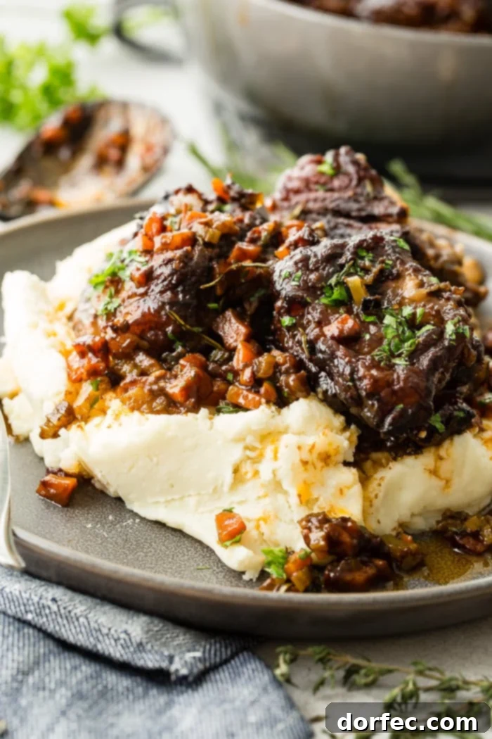 A dark grey plate with a pile of creamy mashed potatoes with fall apart braised beef short ribs and fresh parsley
