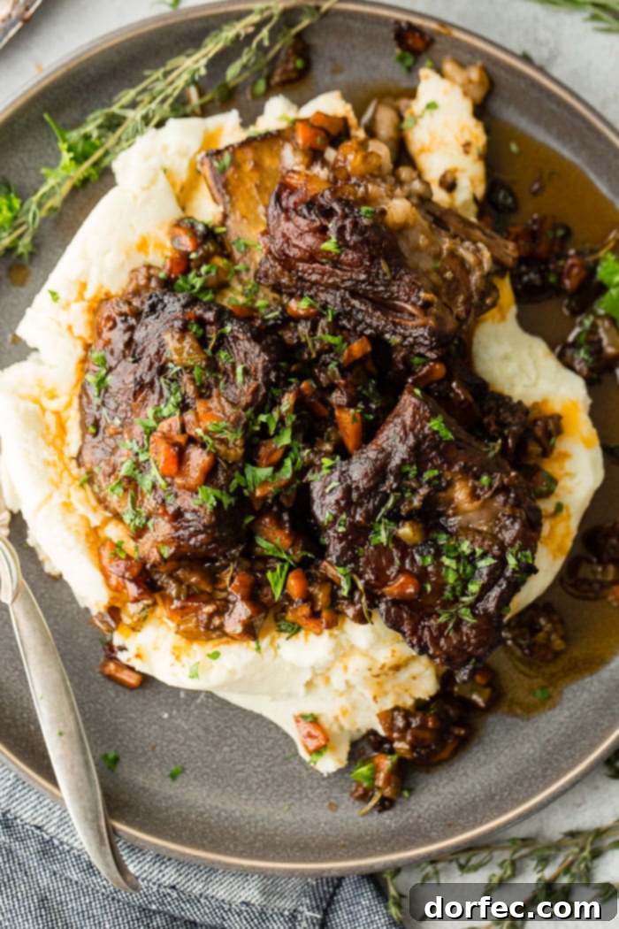A dark grey plate with a pile of creamy mashed potatoes with fall apart braised beef short ribs and fresh parsley