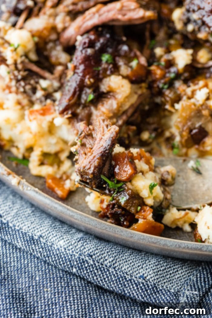 A dark grey plate with a pile of creamy mashed potatoes with fall apart braised beef short ribs and fresh parsley